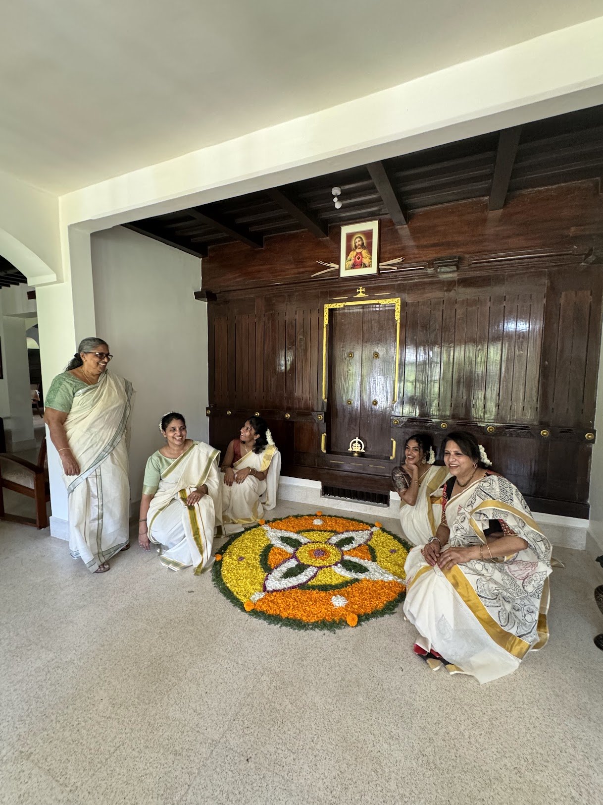 Women of the family in Kerala saris around an Onam pookalam in the hall